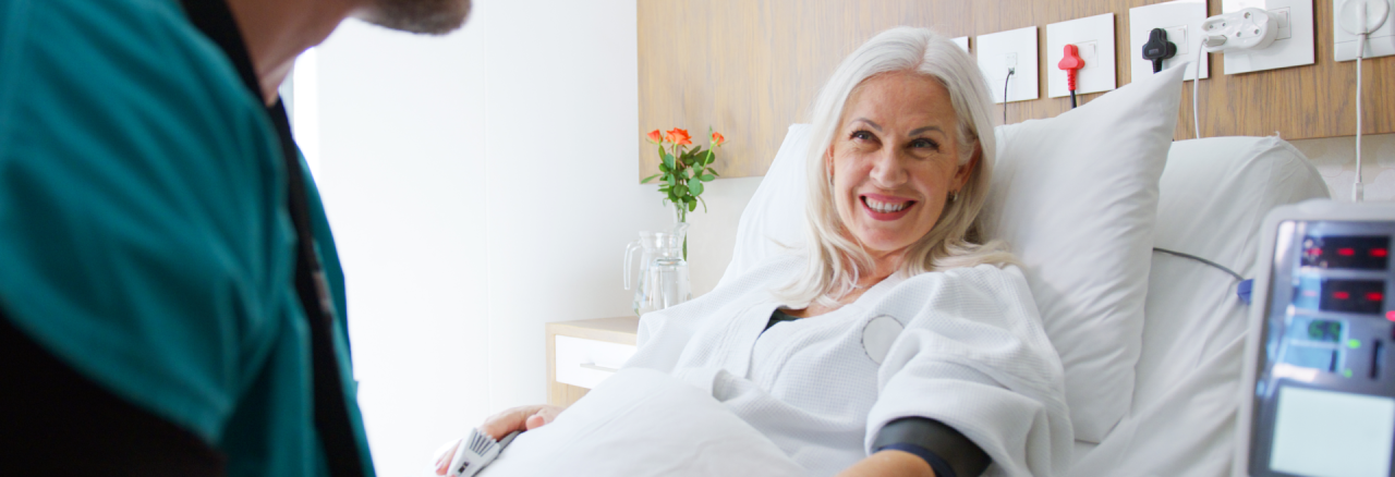 Patient Retention & Referral Management 3 Smiling female patient in hospital bed speaking with healthcare provider, representing positive patient experience and quality care